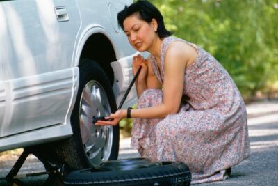 Foto de una mujer reparando el pinchazo de su auto.